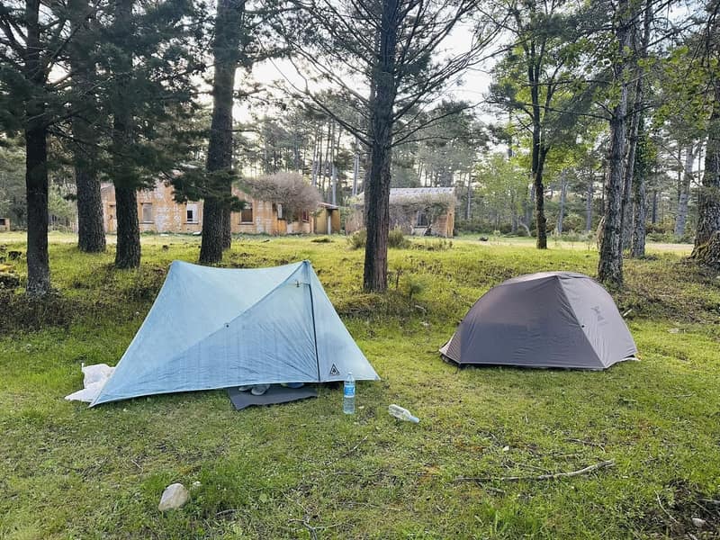 Deux tentes montées côte à côte sous les pins corses près d'un refuge du GR20, une ultralight et une classique